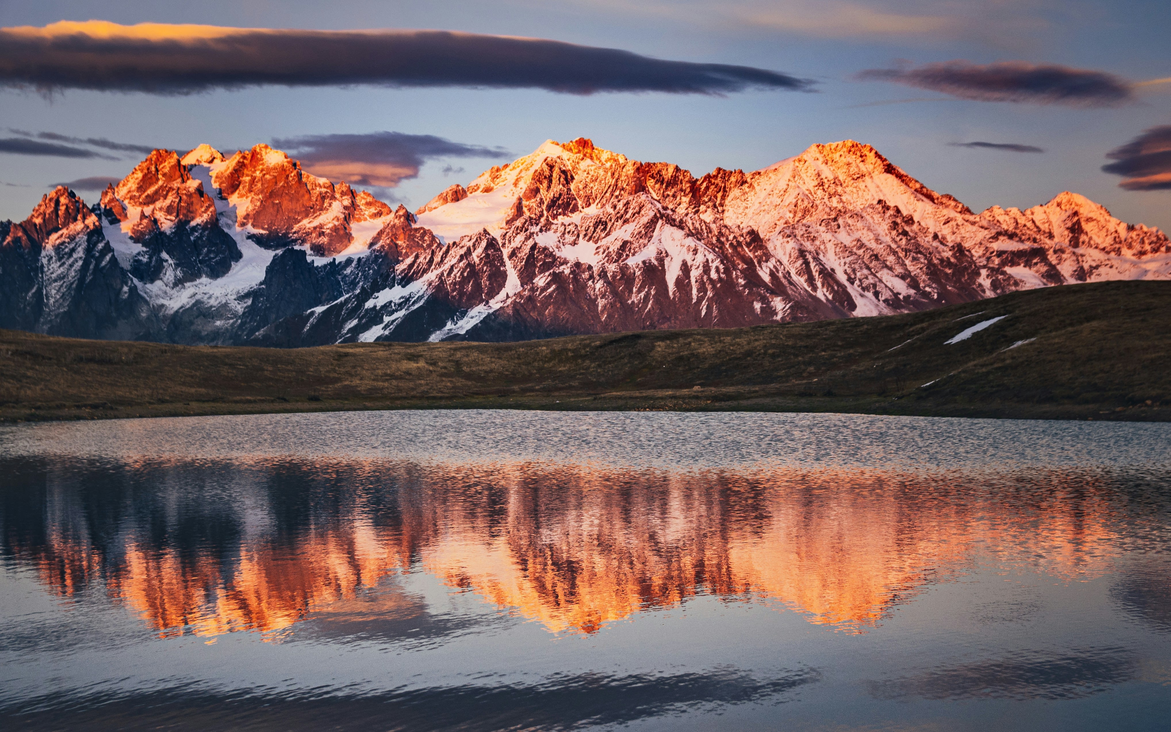 brown and white mountain near lake under gray sky