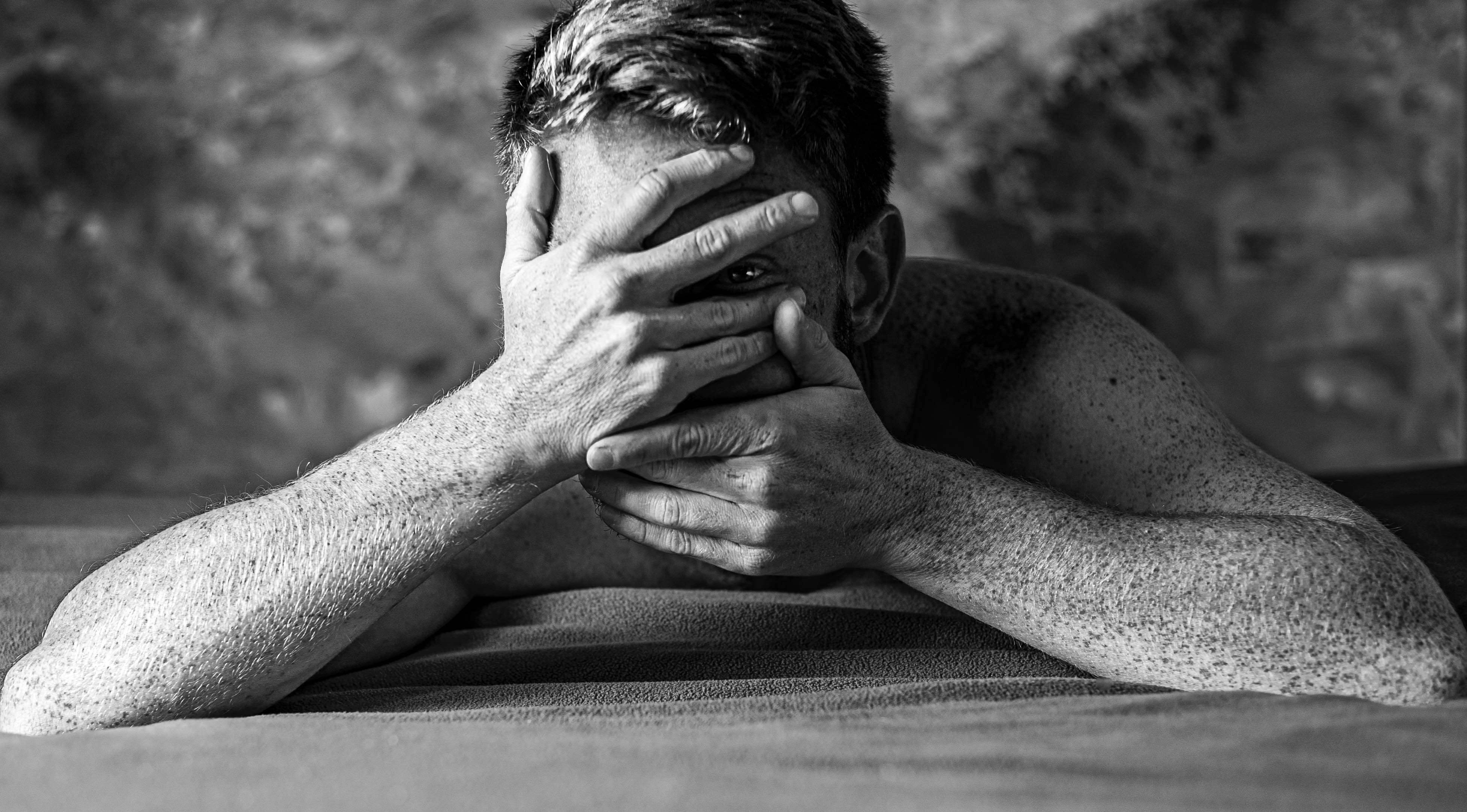 grayscale photo of man covering face with both hands