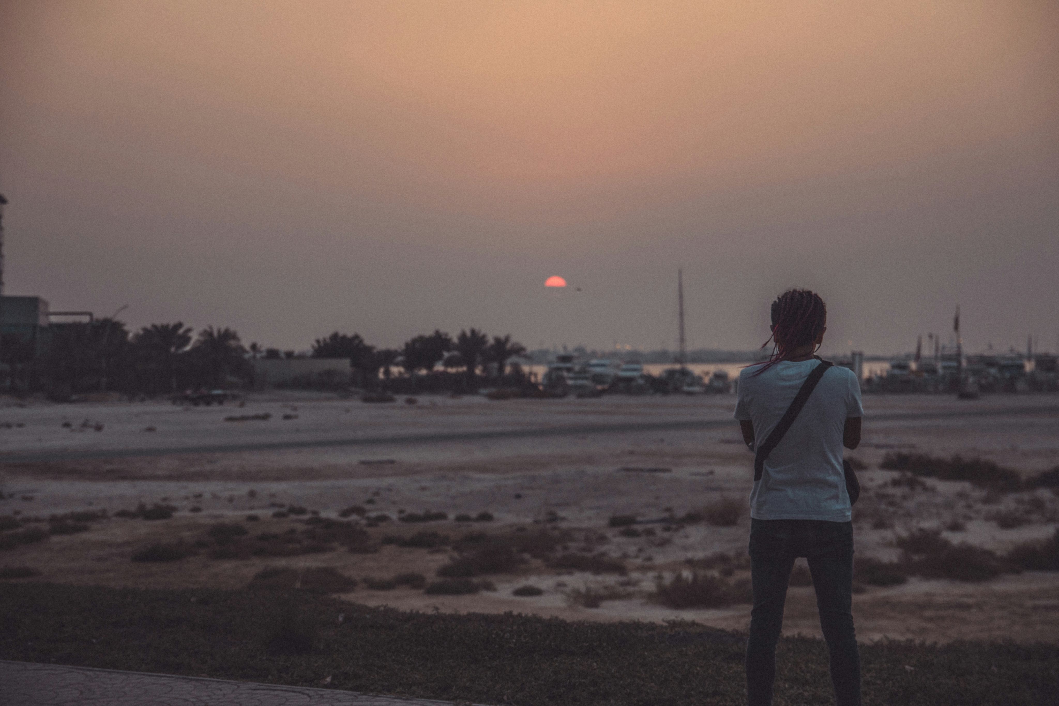 man wearing white t-shirt and blue jeans standing near field during sunset